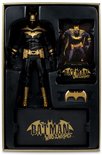Verpakking met een actiefiguur van Batman, een kaart, een vleermuislogo-accessoire en een sokkel, allemaal met zwarte en gouden kleurenschema's.
