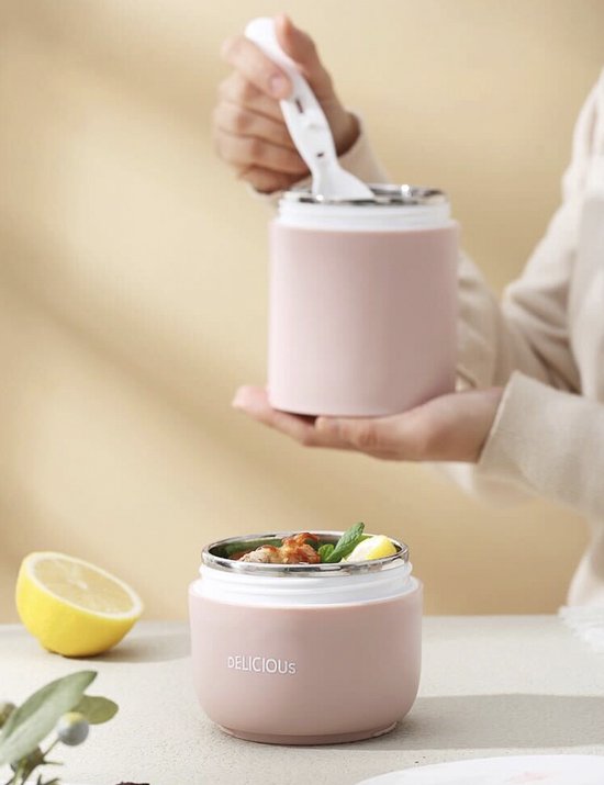 Een hand houdt een roze lunchpot met lepel omhoog. Een andere roze pot staat ernaast.