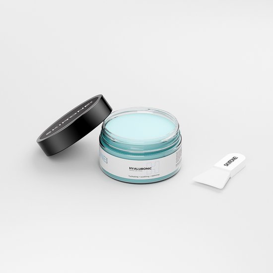 Open glazen pot hyaluronzuur masker met spatel en los deksel op witte achtergrond.