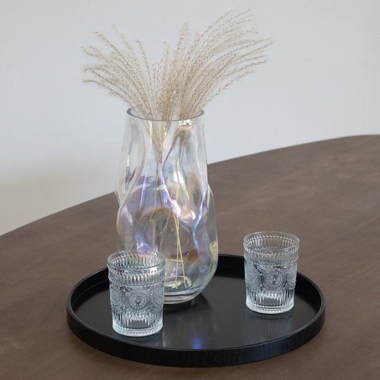Vase en verre avec des herbes séchées sur un plateau noir avec deux verres.