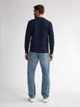 Man staand van achteren, dragend een lichtblauwe loose fit jeans. Zichtbaar zijn de achterzakken met een blauw stiksel.