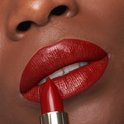 Een vrouw met een donkere huid, volle rode lippen en een gouden L'Oréal lipstick die wordt aangebracht. De lippenstiftkleur is diep rood.