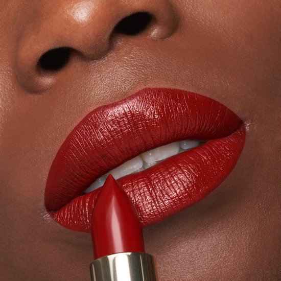 Een vrouw met een donkere huid, volle rode lippen en een gouden L'Oréal lipstick die wordt aangebracht. De lippenstiftkleur is diep rood.