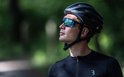 Man met zwarte fietshelm en sportbril met blauwe spiegelglazen, kijkt omhoog.