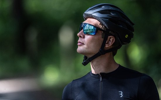 Man met zwarte fietshelm en sportbril met blauwe spiegelglazen, kijkt omhoog.