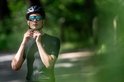 Man met zwarte fietshelm en sportbril met blauwe spiegelglazen, doet helmband vast.