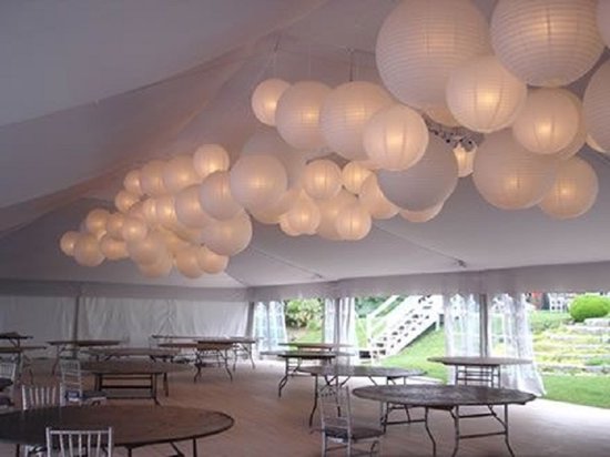 Grote groep witte papieren lampionnen hangt in een tent boven tafels.
