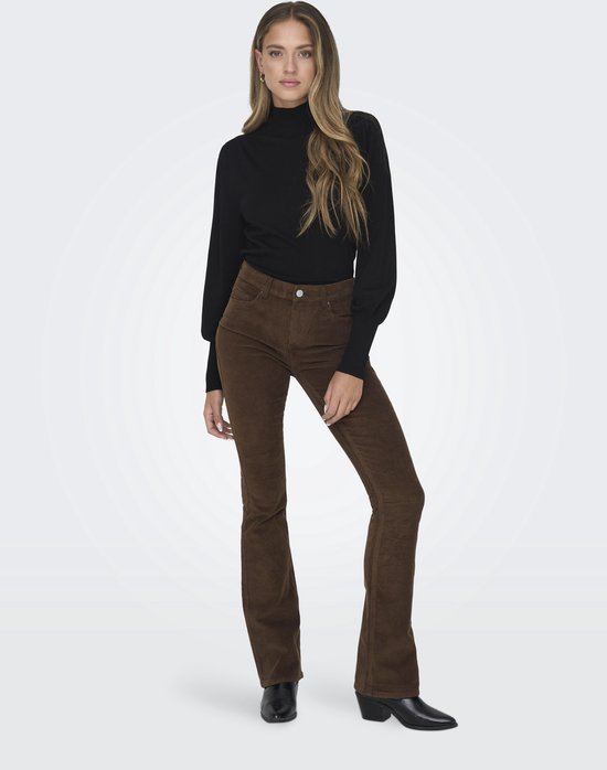 Vrouw in zwarte coltrui en bruine corduroy flare broek, staand, van voren.