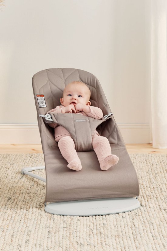 Baby in zandgrijs wipstoeltje, draagt roze trui en sokken.