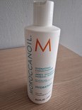 Witte Moroccanoil Hydrating Conditioner fles met oranje M-logo op een houten ondergrond.