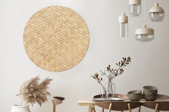 Décoration murale ronde en rotin avec motif tressé, suspendue à un mur blanc au-dessus d'une table en bois.