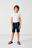 Jongen met donkerblauwe shorts en witte t-shirt, staand.