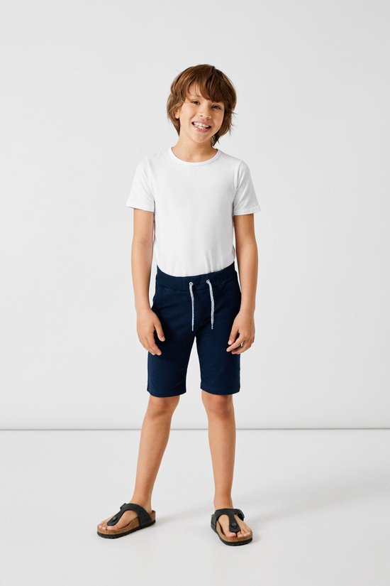 Jongen met donkerblauwe shorts en witte t-shirt, staand.