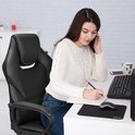 Een vrouw met een witte trui zit op een zwarte bureaustoel, schrijft in een notitieboekje, met een computer op het bureau.