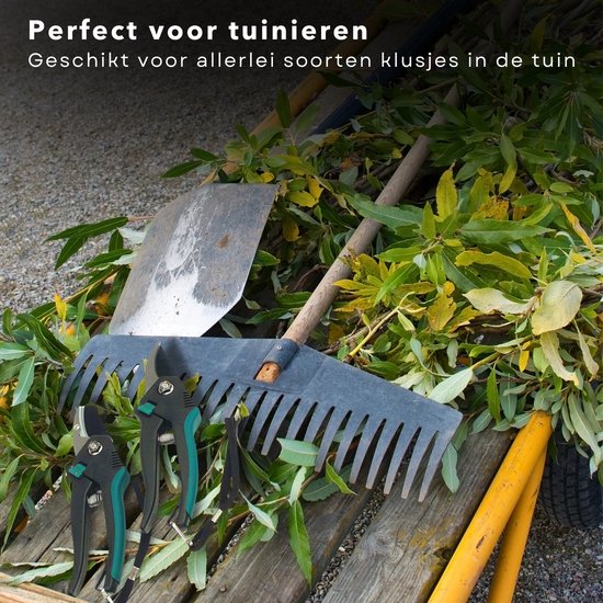Zwarte snoeischaren met groene accenten op een stapel snoeiafval naast een hark en schep.