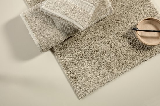 Een beige badmat met twee gevouwen badhanddoeken en een houten schaaltje met zwarte tandenborstel.