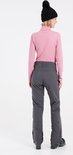 Femme portant un col roulé rose et un pantalon de ski gris, avec un bonnet noir.