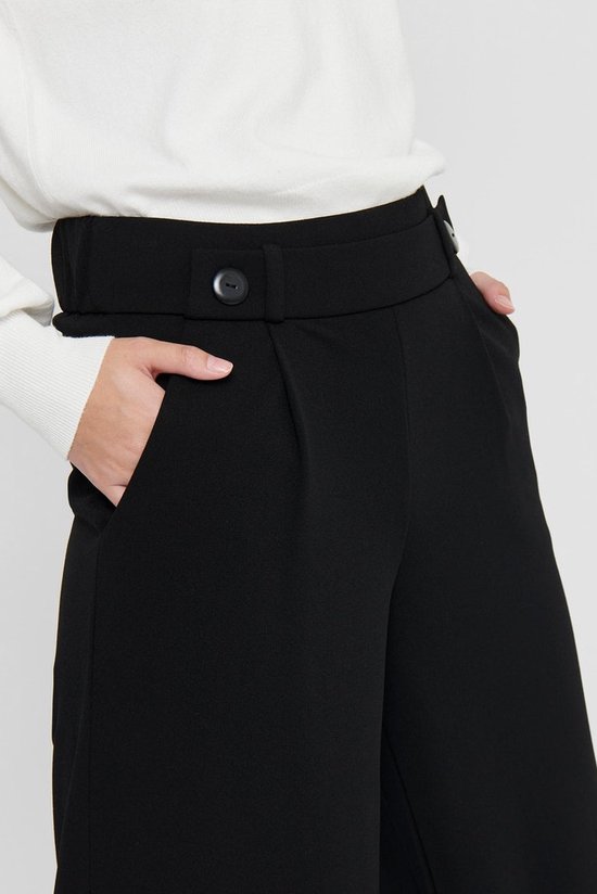 Detail van zwarte wijde broek met knoop- en steekzakdetails aan de voorkant.