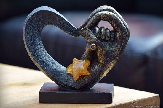 Zwarte hartvormige urn met gouden handen, met een amberkleurige glazen ster.