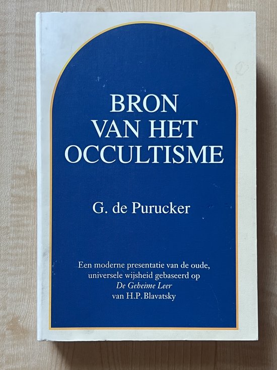 Boek 'Bron van het Occultisme' door G. de Purucker. Blauwe omslag met witte tekst en oranje/gouden rand.
