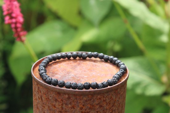 Donkergrijze lavasteen armband op roestige metalen object met groene achtergrond.