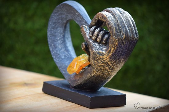Zwarte hartvormige urn met gouden handen, met een amberkleurige glazen ster.