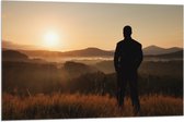 Vlag - Silhouet van Man kijkend naar Zonsondergang in Landschap - 105x70 cm Foto op Polyester Vlag
