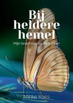 Een oranje-bruine vlinder met zwarte lijnen op de vleugels, zittend op een blauw oppervlak. Tekst: 'Bij heldere hemel - Mijn leven voorbij de kanker - Minke Koks'.
