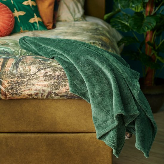 Donkergroene plaid met een zachte, pluizige textuur, gedrapeerd over een bed met een natuurprint dekbed.