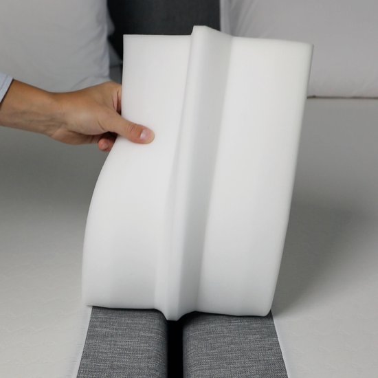 Hand houdt een witte, schuimrubberen matraswig vast, met een inkeping aan de onderkant.