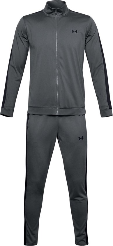 Grijs Under Armour trainingspak met zwarte strepen op de mouwen en zijkanten van de broek. Zwarte logo's.