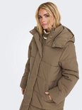 Een vrouw met blond haar draagt een lange, bruine pufferjas met capuchon.