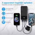 Zwarte powerbank laadt tegelijkertijd smartphone, koptelefoon en oordopjes op.