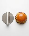 RVS smash burger pers naast een dubbele smash burger met gesmolten kaas, gefotografeerd van bovenaf.