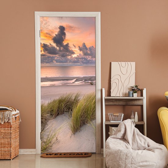 Deursticker met zonsondergang, strand en duingras, in een kamer met bruine muren.