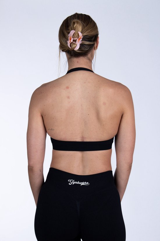 Achterkant van een vrouw in zwarte sportbeha en legging, met een bloem in haar opgestoken haar.
