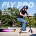 Meisje met helm en spijkerbroek stunt op een regenboogkleurige "Fly Pro" step in een skatepark.