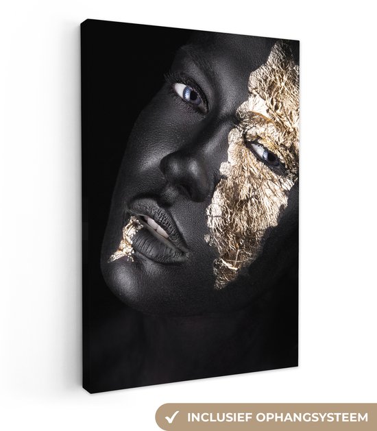 Een vrouwelijk gezicht met zwarte bodypaint en gouden bladfolie op de helft van het gezicht, met blauwe ogen.