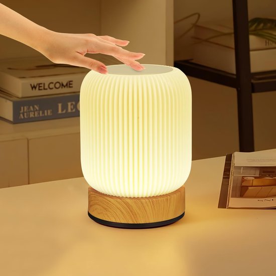 Lampe de table côtelée jaune avec base en bois, touchée par une main.