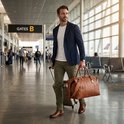 Man met blauwe blazer en bruine tas loopt door een moderne luchthaven bij Gate B.