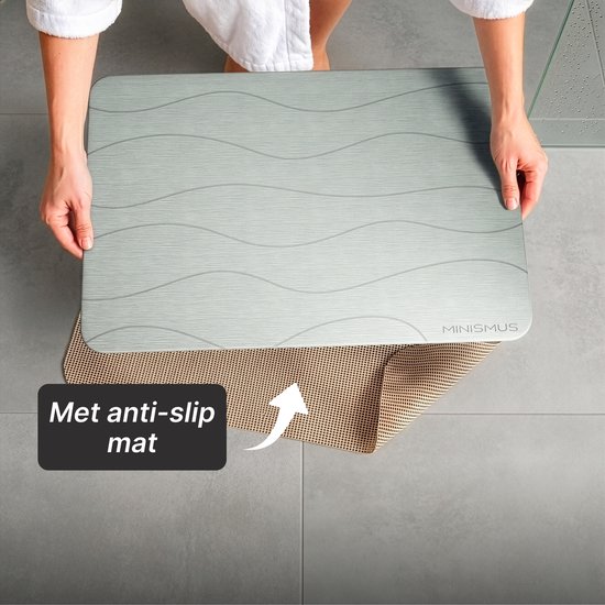 Tapis de bain MINISMUS gris à motif ondulé tenu au-dessus d'un tapis antidérapant.