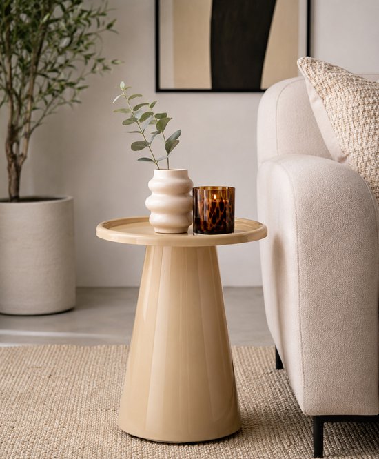 Beige glanzende bijzettafel naast een bank, met vaas en kaars erop.