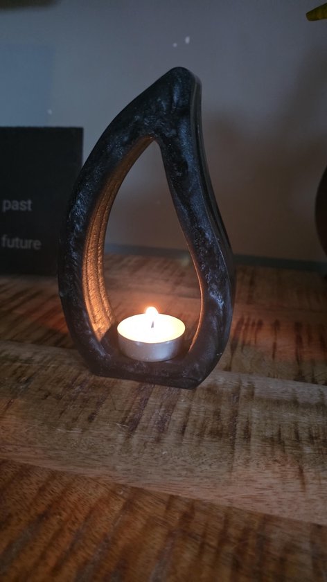 Zwarte, druppelvormige kandelaar met een brandende theelichtje erin, geplaatst op een houten ondergrond.