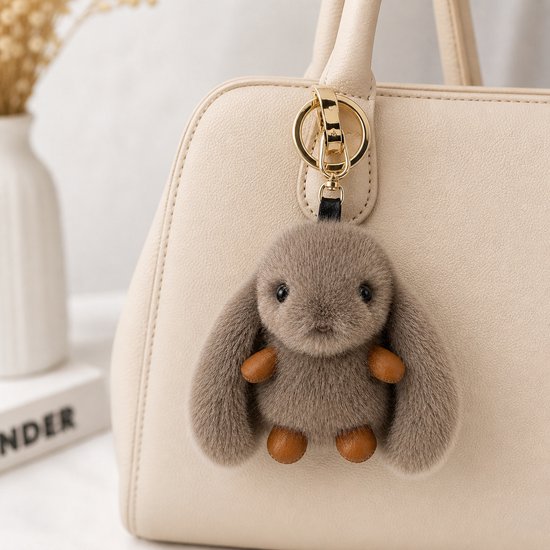Donkergrijze pluche konijn sleutelhanger met bruine details, hangend aan een beige tas.