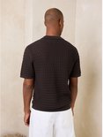 Achterkant van een man in een bruin poloshirt met visgraatpatroon.