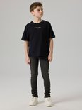 Jongens model in een donkergrijze slim fit jeans en een zwarte t-shirt.