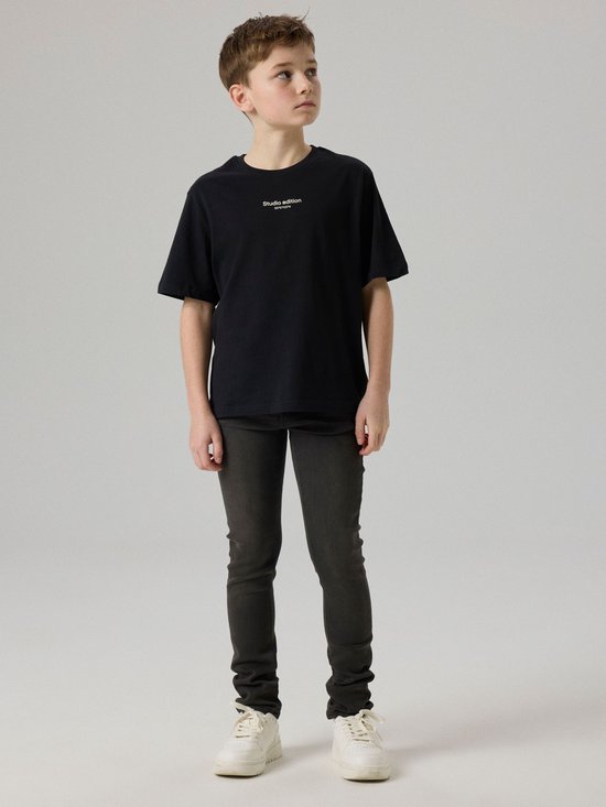 Jongens model in een donkergrijze slim fit jeans en een zwarte t-shirt.