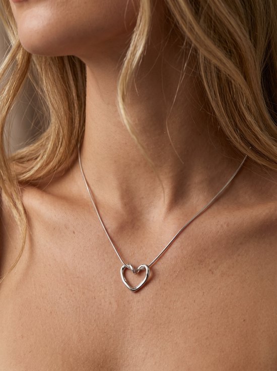 Model draagt een zilverkleurige hartvormige ketting om de hals.