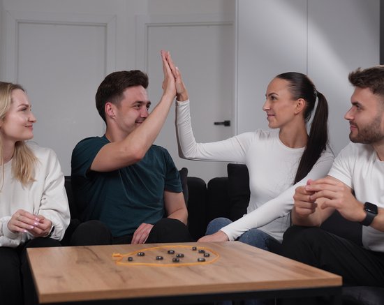 Twee spelers van een magnetenspel geven elkaar een high-five, anderen kijken toe.