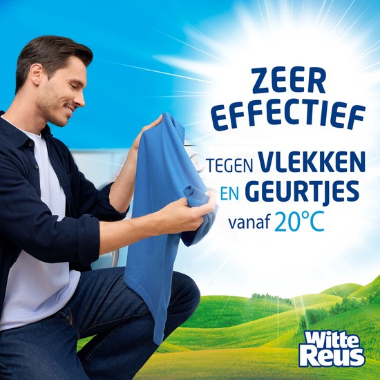 Man houdt een blauw shirt omhoog voor een wasmachine, met groene heuvels op de achtergrond.